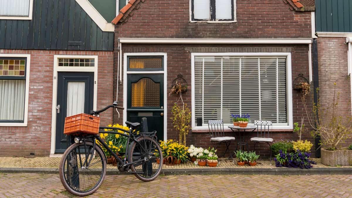 De gevels van drie typisch Nederlandse tussenwoningen. Op de voorgrond staat een fiets. Voor de middelste woning zijn planten zichtbaar.